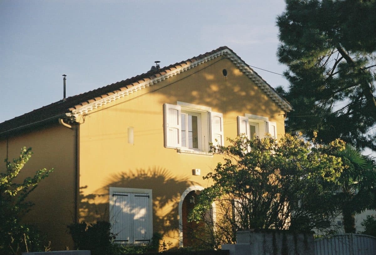 Une maison jaune aux volets blancs