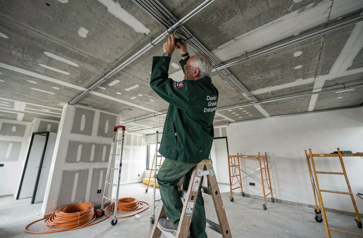 Électricien de Daniel Gravier Entreprises posant des conduits électriques au plafond d'un chantier de bureaux